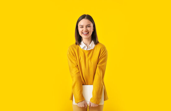 Beautiful young woman with laptop on yellow background