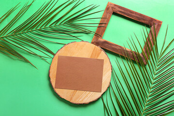 Composition with blank card, empty picture frame and palm leaves on color background