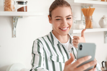 Young woman with mobile phone video chatting in kitchen