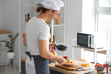 Male chef adding tasty sauce into plate with pasta in kitchen