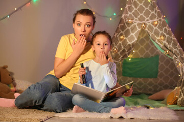 Shocked little girl and her mother reading fairy-tale late in evening at home