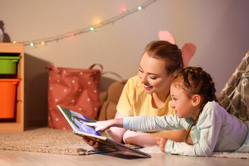 Little girl with her mother reading fairy-tale late in evening at home