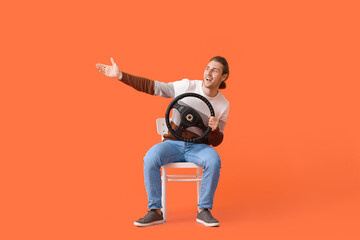 Young man with steering wheel sitting on chair against color background