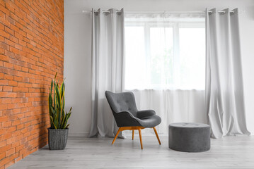 Modern armchair and pouf near window in room