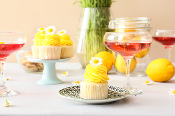 Tasty cupcakes, glasses of drink and chamomile flowers on table in room