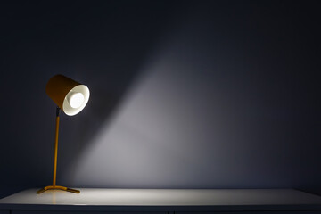 Glowing lamp on table near wall in dark room