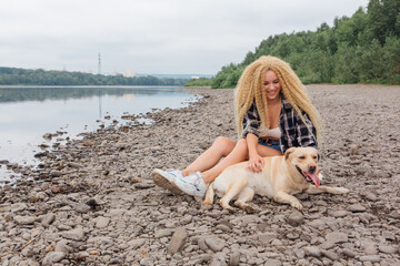 Young woman sitting with her labrador retriever dog on the river shore