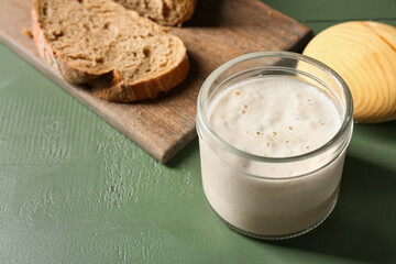 Glass jar with sourdough on green wooden background