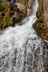 Close-up of a powerful waterfall in high quality. Side view of a sun-drenched waterfall in the wild. A large stream of water pours down from the mountain.