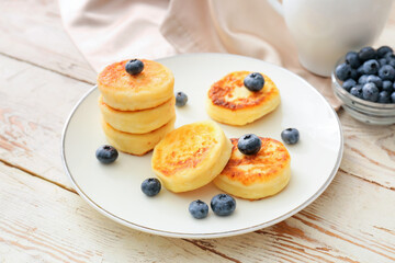 Plate with cottage cheese pancakes and blueberries on light wooden background