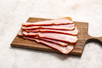 Wooden board with slices of tasty smoked bacon on light background