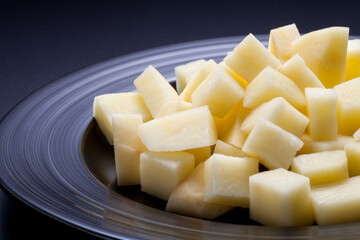 Chopped raw potatoes in a black plate on black background. Close-up.