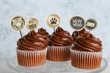 Dessert stand with tasty cupcakes for New Year 2022 celebration on light background