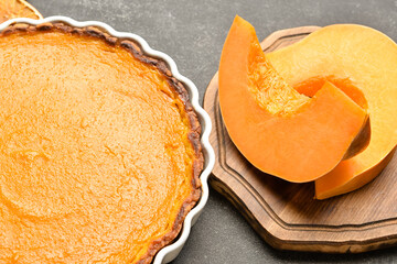 Baking dish with tasty pumpkin pie and fresh vegetable on black background, closeup
