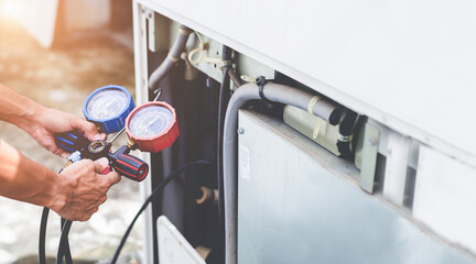 Air repair mechanic using measuring equipment for filling industrial factory air conditioners and checking maintenance outdoor air compressor unit.