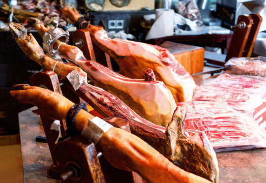 Legs of delicious Spanish jamon fixed on wooden jamoneras ready for sale in small shop