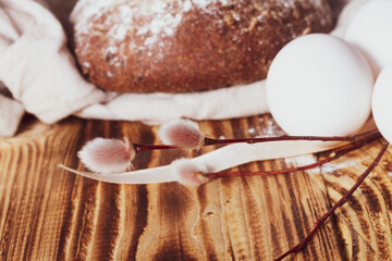 Simple Easter rustic background with a willow twig, white chicken eggs and grain bread on a brown wooden table