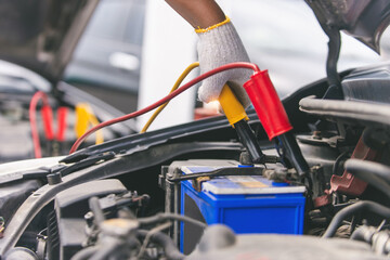 Close up of hand Charging car battery with electricity trough jumper cables, copy space for text.