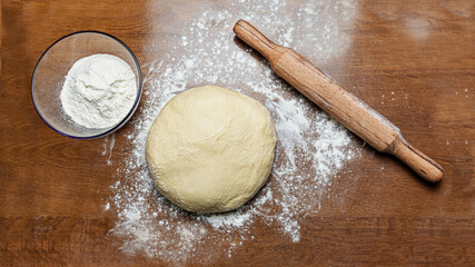 Ball of dough on a wooden background with flour dust. Rolling pin, flour and dough are on the table.
raw fresh dough for baking in home kitchen. dough without eggs

