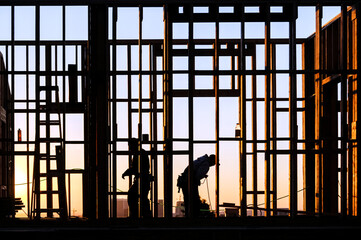 Obraz na płótnie Canvas Framing carpenters building walls silhouetted by morning sunlight