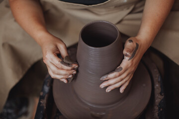 Fototapeta na wymiar A middle-aged plus size woman in a pottery apron creates a clay vase on a potter's wheel in a pottery workshop