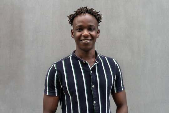 Portrait of a handsome Black African American young male smiling in a grey concrete background. Cool millennial man looking to the camera. 