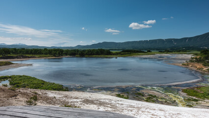 Blue lake in the caldera of an extinct volcano. The water off the coast is yellow-green due to thermophilic microorganisms and algae. A mountain range against the sky. Kamchatka. Uzon