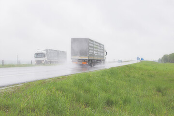 Fototapeta na wymiar The movement of trucks of trucks with a semi-trailer and cars on a wet road in rain and fog and in poor visibility. Road safety concept. Copy space for text