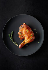 Grilled chicken leg sprinkled with rosemary on a black plate.