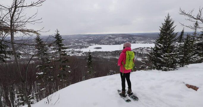 Snowshoeing people in winter forest with snow covered trees on snowy day. Woman on hike in snow hiking in snowshoes living healthy active outdoor lifestyle. Mont Tremblant, Laurentians, Quebec, Canada