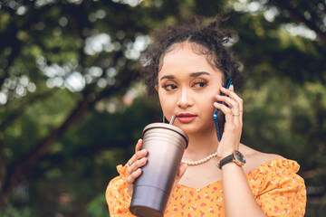 A young asian woman listening attentively or inquiring on the phone while taking a sip from her tumbler.