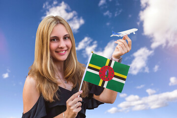 Girl holds flag of Dominica and toy plane on the sky background Concept of air travel and tourism 