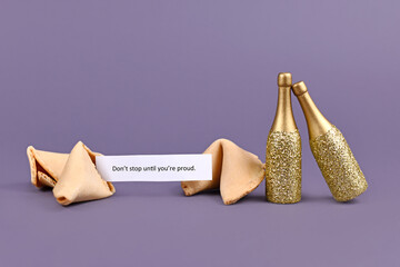 Motivational text 'Don't stop till you're proud' on paper next to champagne bottles