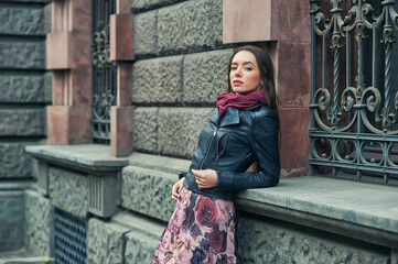A stylish young girl in a fashionable leather jacket on a city street .