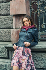 A stylish young girl in a fashionable leather jacket on a city street .
