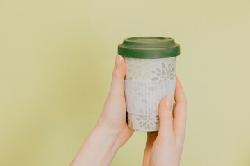 Hands holding bamboo reusable cup with lid on. Reusable tea cup on a green background. Zero waste....