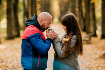 Fototapeta premium A married couple with a hot drink in the autumn park. The concept of love and relationships