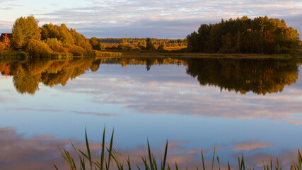 Picturesque rural landscape - a lake with smooth water in which the sky and trees are reflected