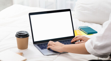 Fototapeta na wymiar Woman using and typing on Laptop with a mockup white screen on bed.