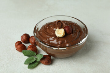 Bowl with chocolate paste, nuts and mint on white textured background