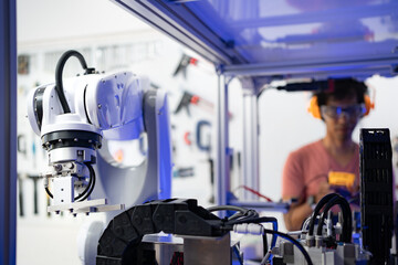 Close-up of a modern automation robotic arm machine for multiple industrial applications in manufacturer factory with a blurred background of Caucasian male engineer standing working in the back.