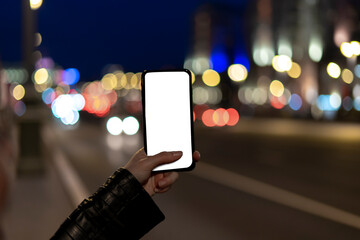 Female hands holding blank screen smartphone at street night in city.