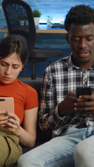 Interracial couple holding smartphones in living room on couch. Modern multi ethnic people with technology sitting together at home on sofa. Husband and wife using phone devices