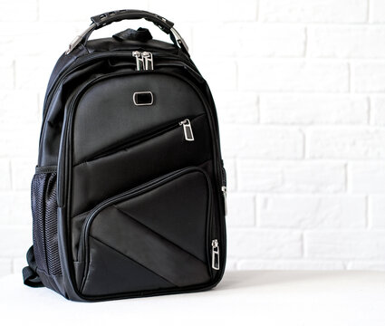 black backpack for student or adventure against white brick wall background with copy space