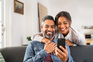 Happy indian couple using smartphone at home - Powered by Adobe