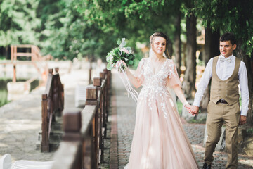 Stylish couple of happy newlyweds walking in the park on their wedding day with bouquet