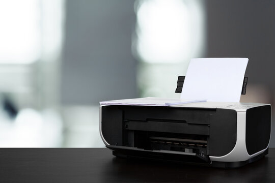 Compact laser printer on black desk against blurred background