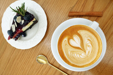 a cup of latte art coffee with blueberry cheesecake on wooden table 