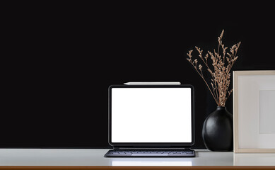 Blank screen tablet with magic keyboard and wooden frame on white table and black background.