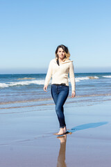 woman walking on the beach looking at camera with decision dressed in a wool sweater and jeans